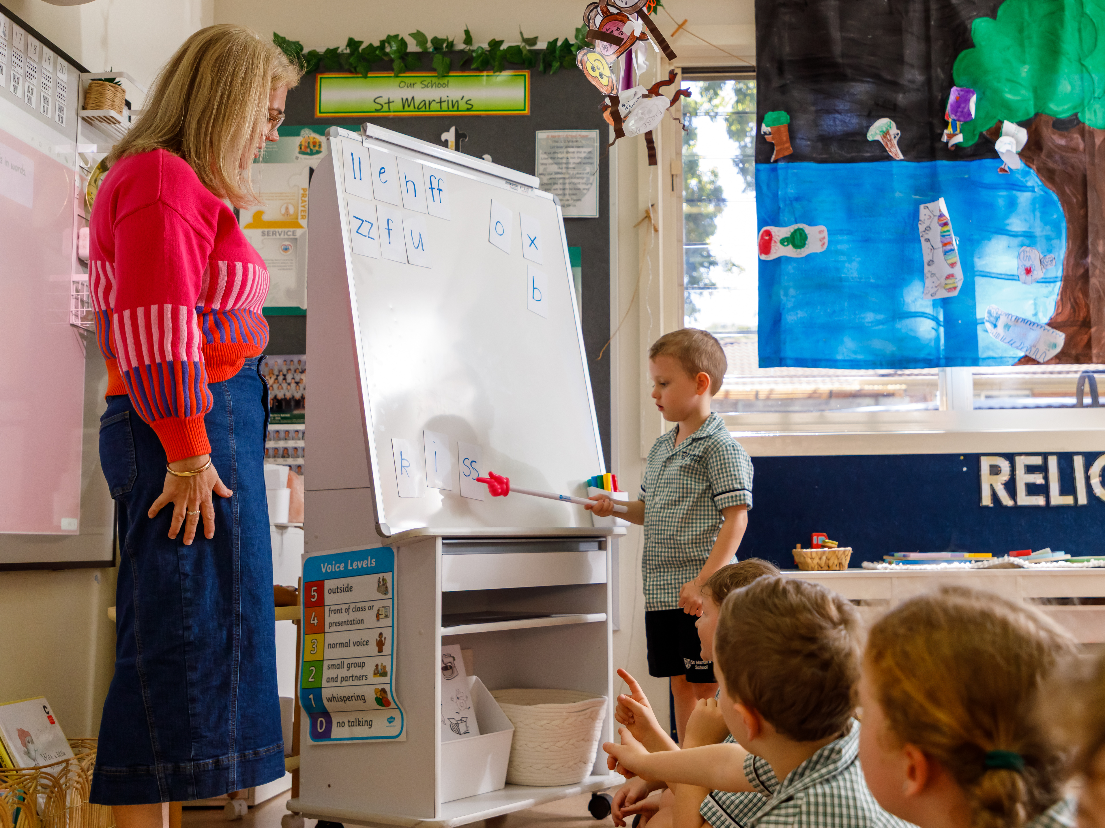 Boy standing in front of a classroom pointing a ruler at a whiteboard.