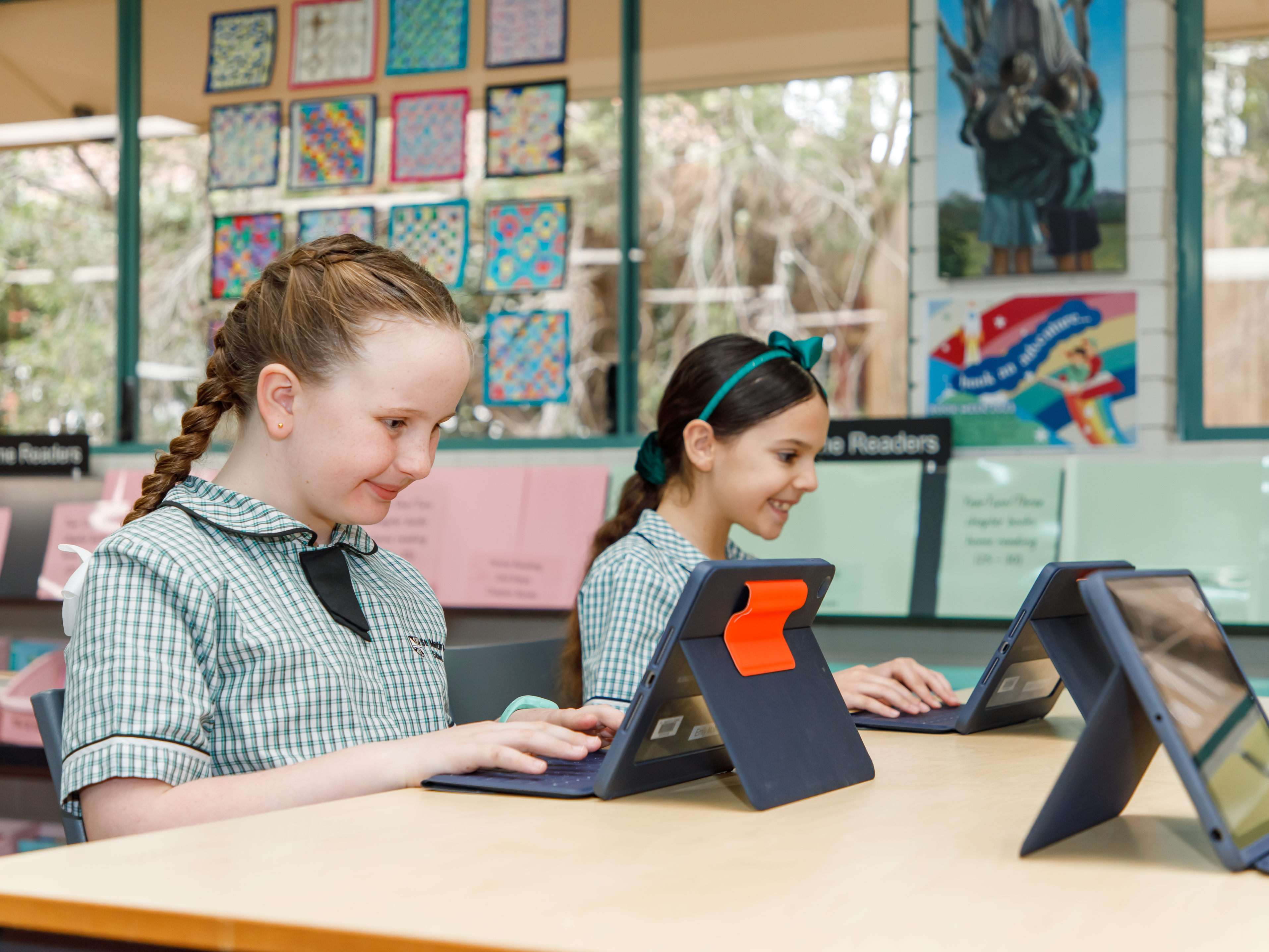 Two primary aged students, sitting at their desk with laptops.