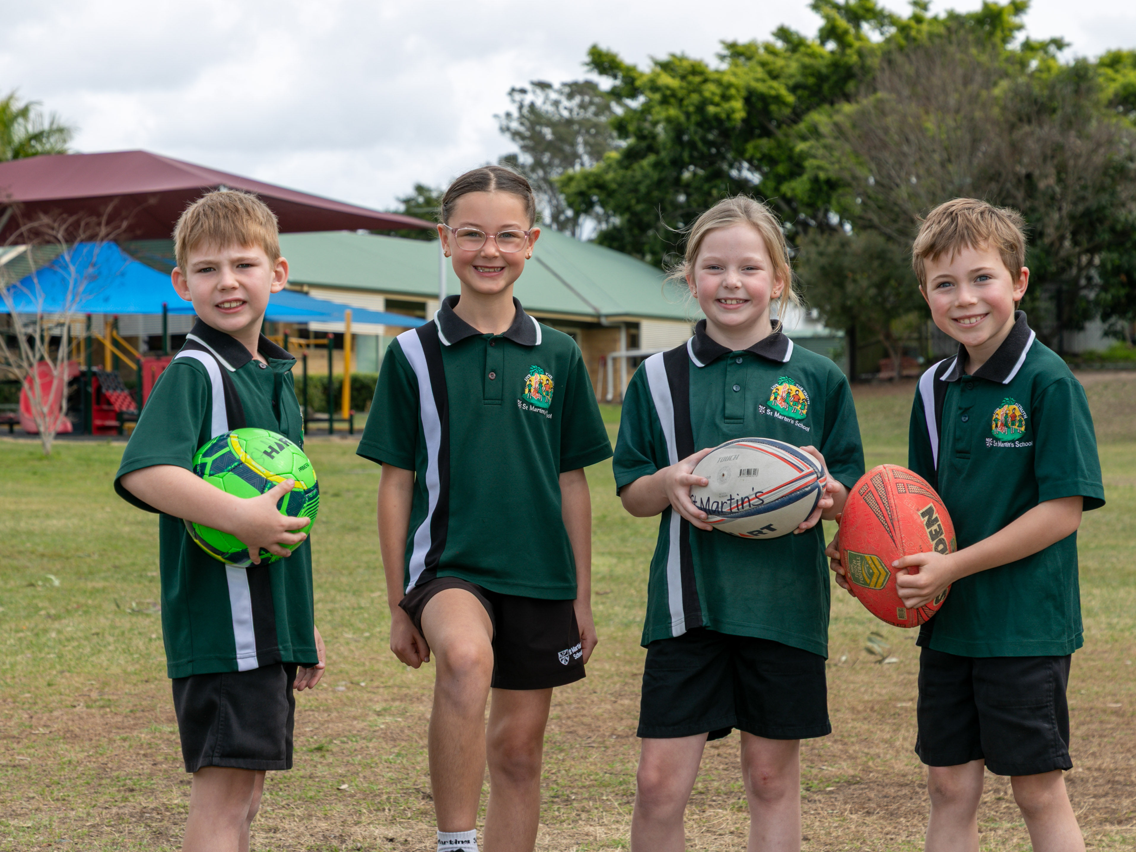 Four primary aged students in sport uniforms facing towards the camera and smiling. 