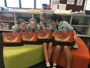 Four students sitting on stools in the library, with their laptops.