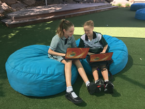 Two students sitting on blue beanbags, outside with their laptops.