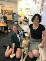 A student and adult sitting in a classroom with a large dog between them.