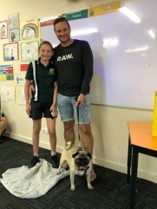Student and adult standing in a classroom with a small dog on a blanket on the floor.